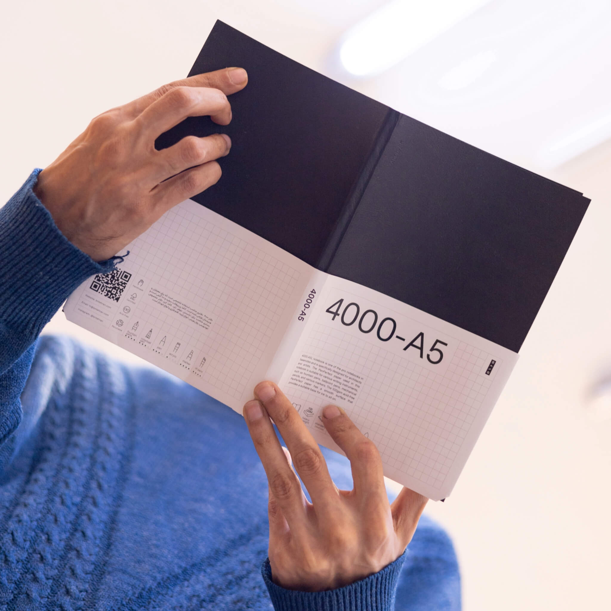 Person holding a basenotes 4000 A5 Notebook with its white branded sleeve, highlighting minimalist grid design and product details.