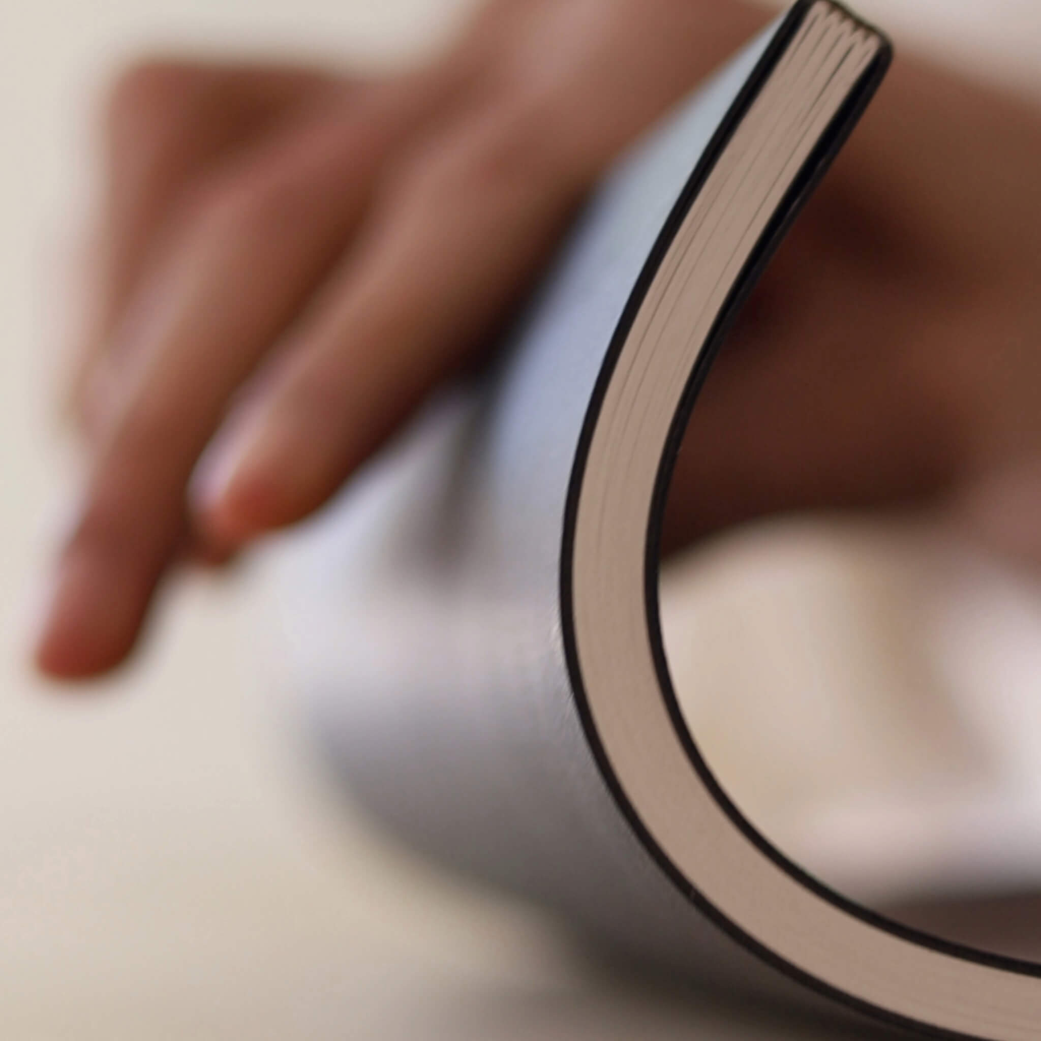 Person bending the basenotes 4000 A5 Notebook slightly to show its flexibility and stitched binding structure.