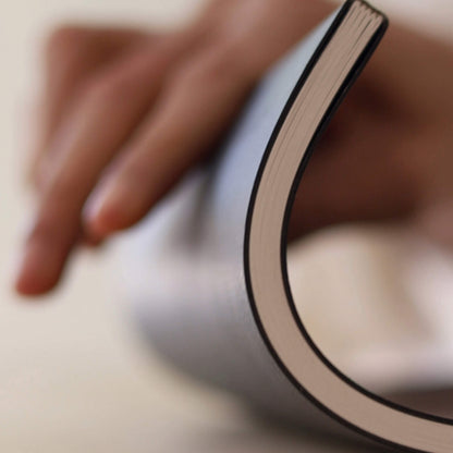 Person bending the basenotes 4000 A5 Notebook slightly to show its flexibility and stitched binding structure.
