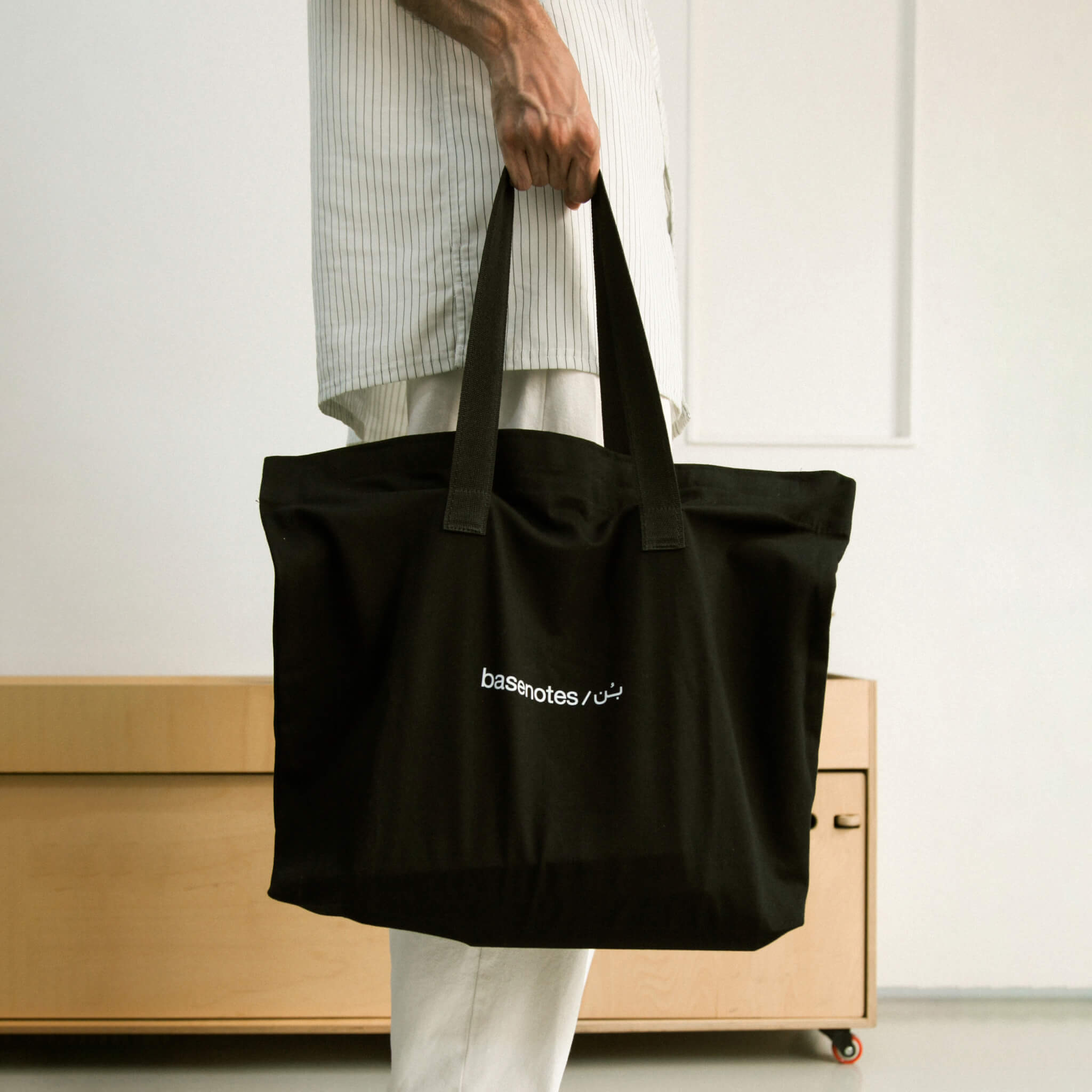 basenotes premium black fabric tote bag carried by hand in a clean, modern interior