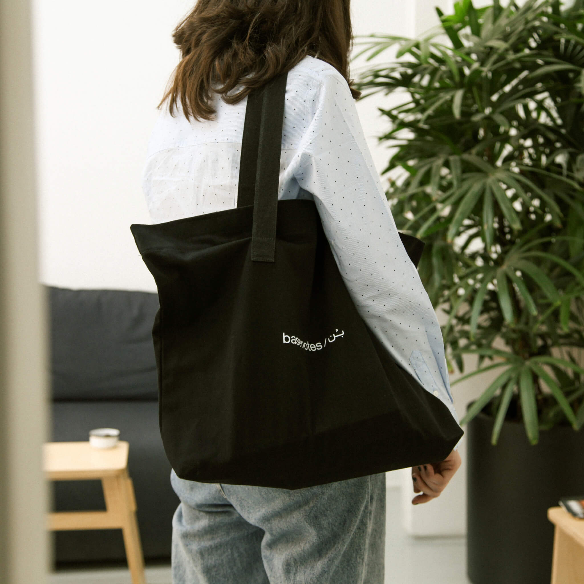 basenotes premium fabric tote bag in black, worn on the shoulder in a relaxed lifestyle setting