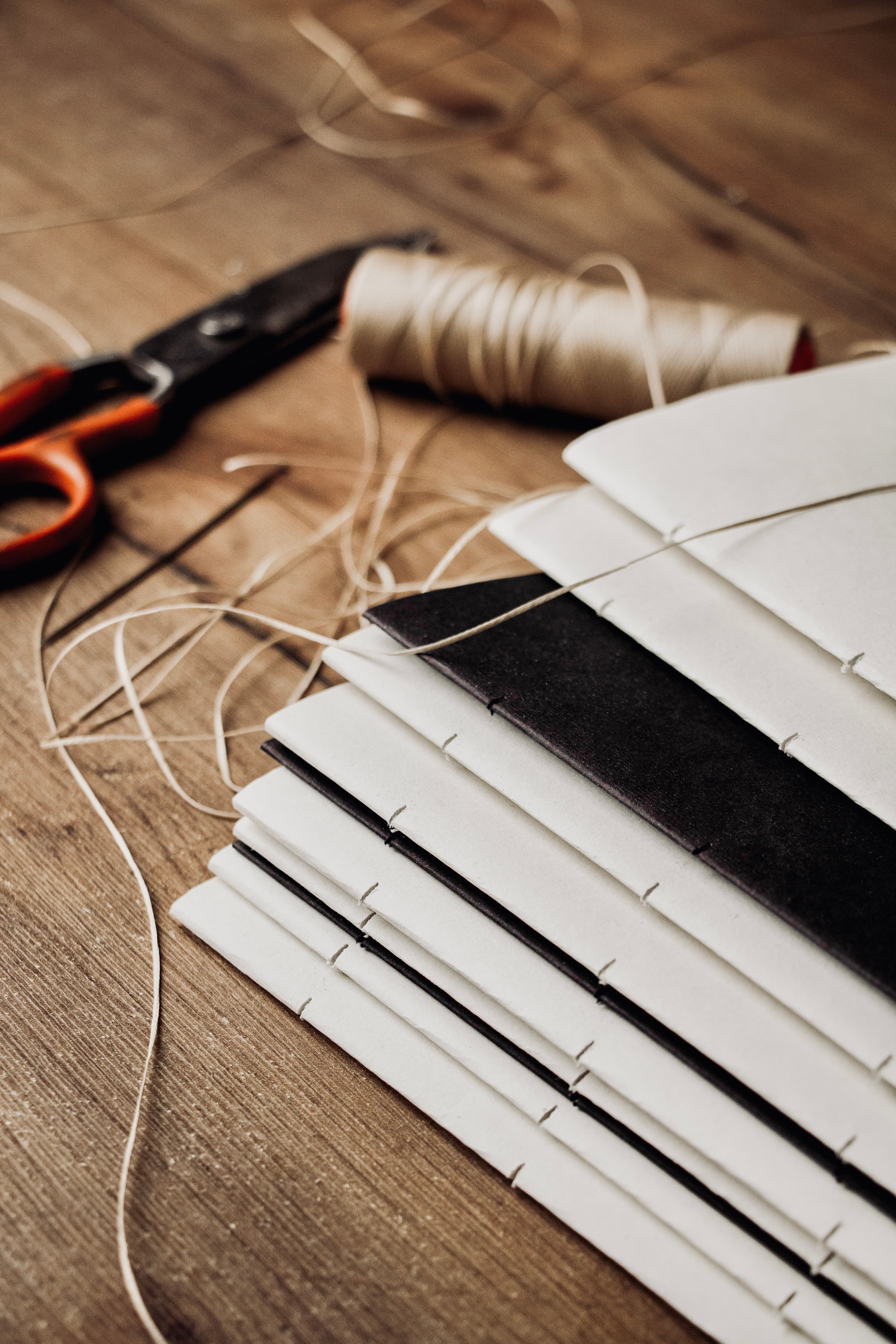 Hand-stitched bookbinding process with thread, needle, and stacked paper notebooks by basenotes.