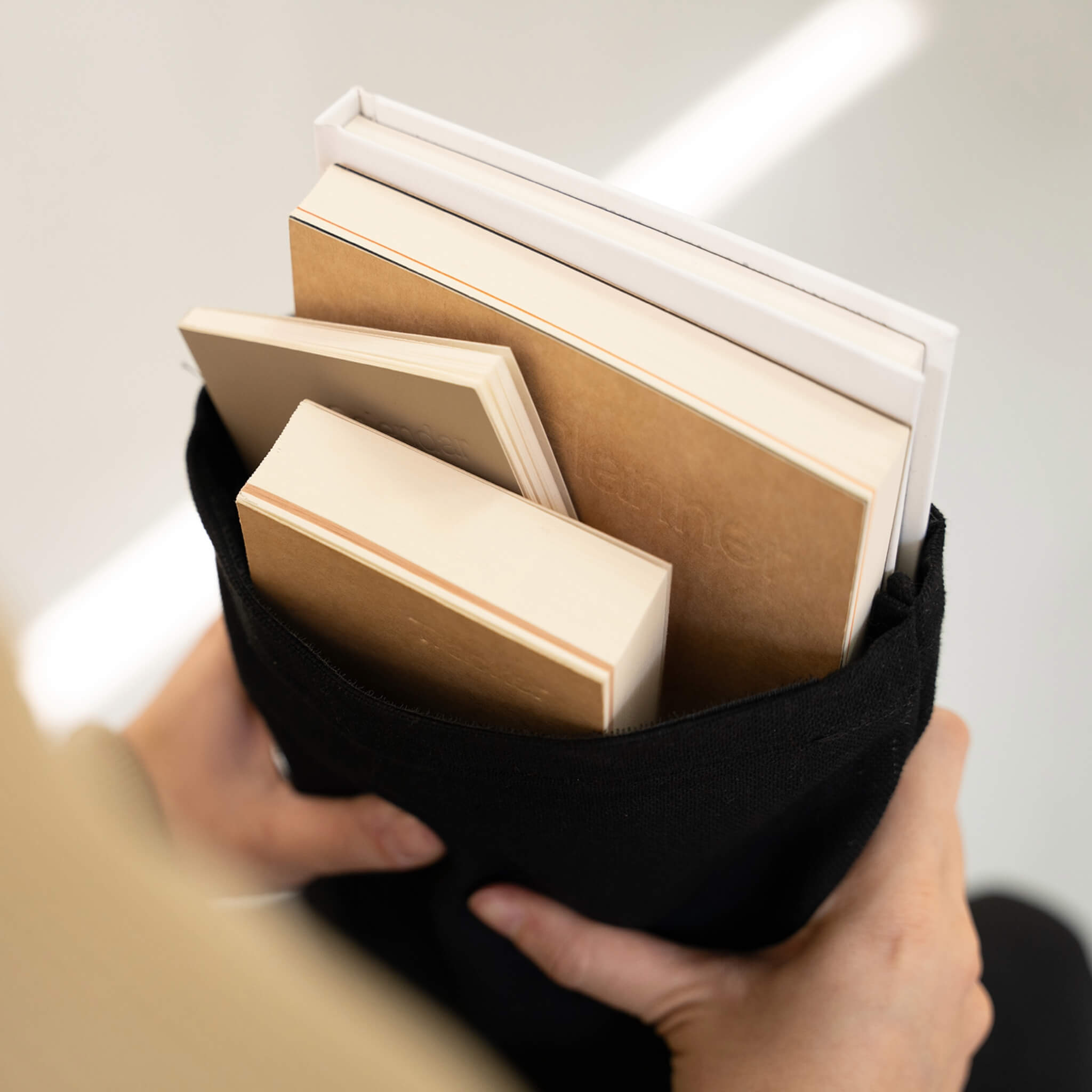 Basenotes black fabric notebook cover carrying A4 and A5 notebooks, shown at an angle while held