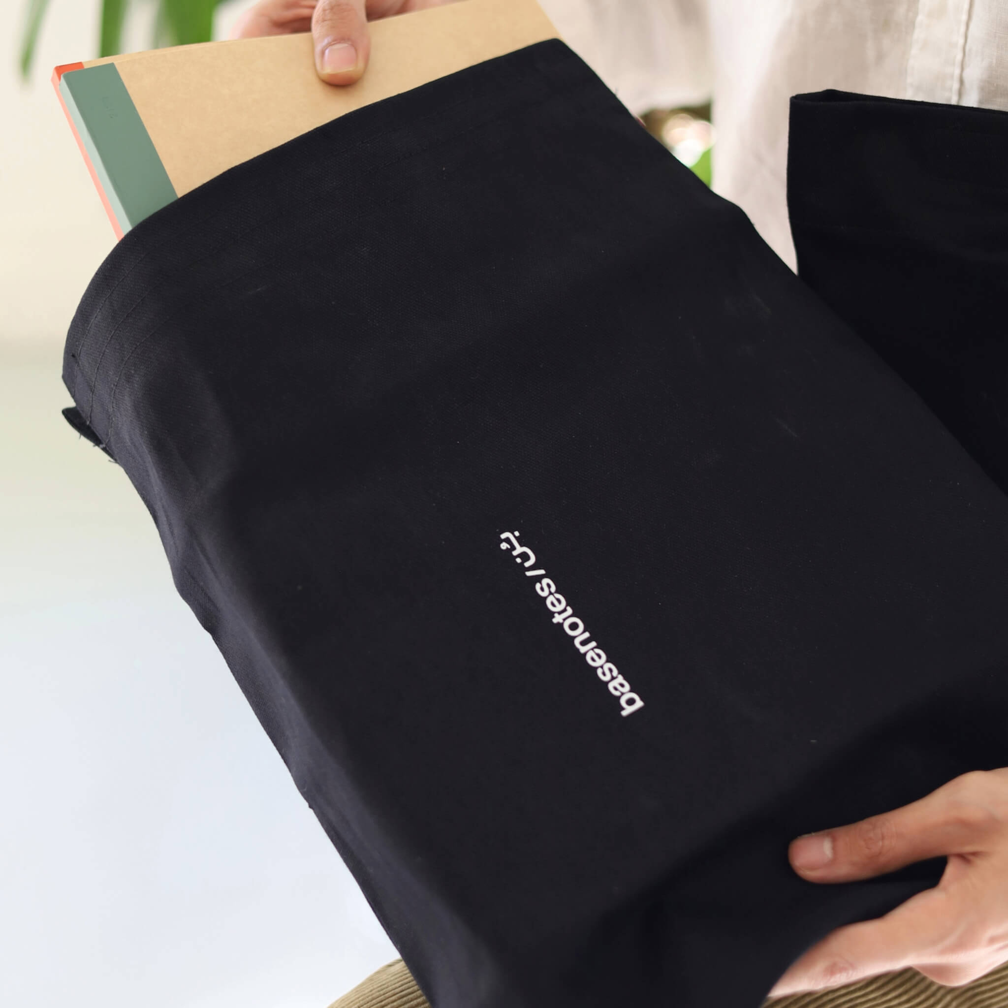 Basenotes black fabric notebook cover with logo visible, holding an A4 or A5 notebook while being carried