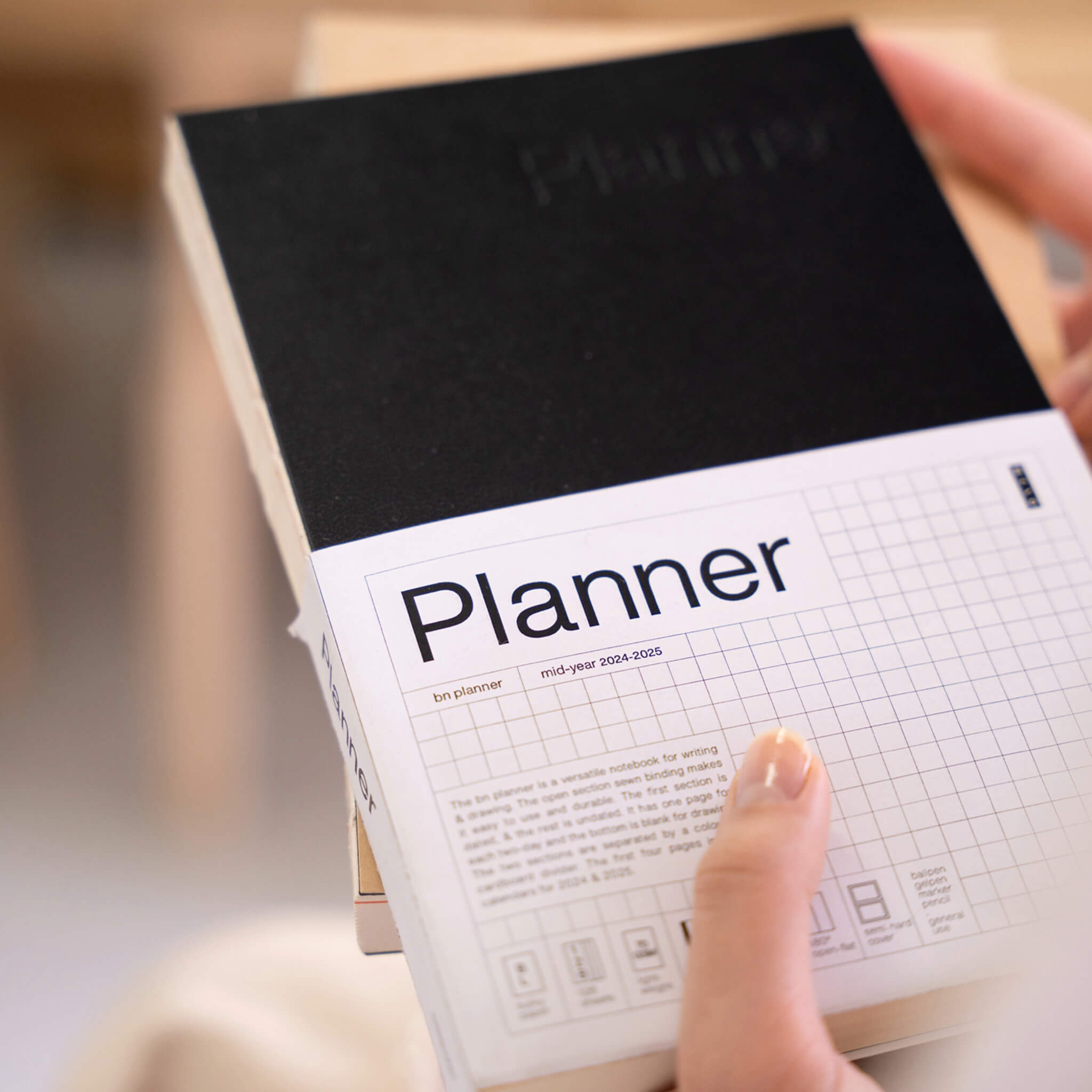 Close-up of the basenotes Planner with black cover and mid-year 2024–2025 label, held in hand crafted with FSC-certified paper for mindful planning.