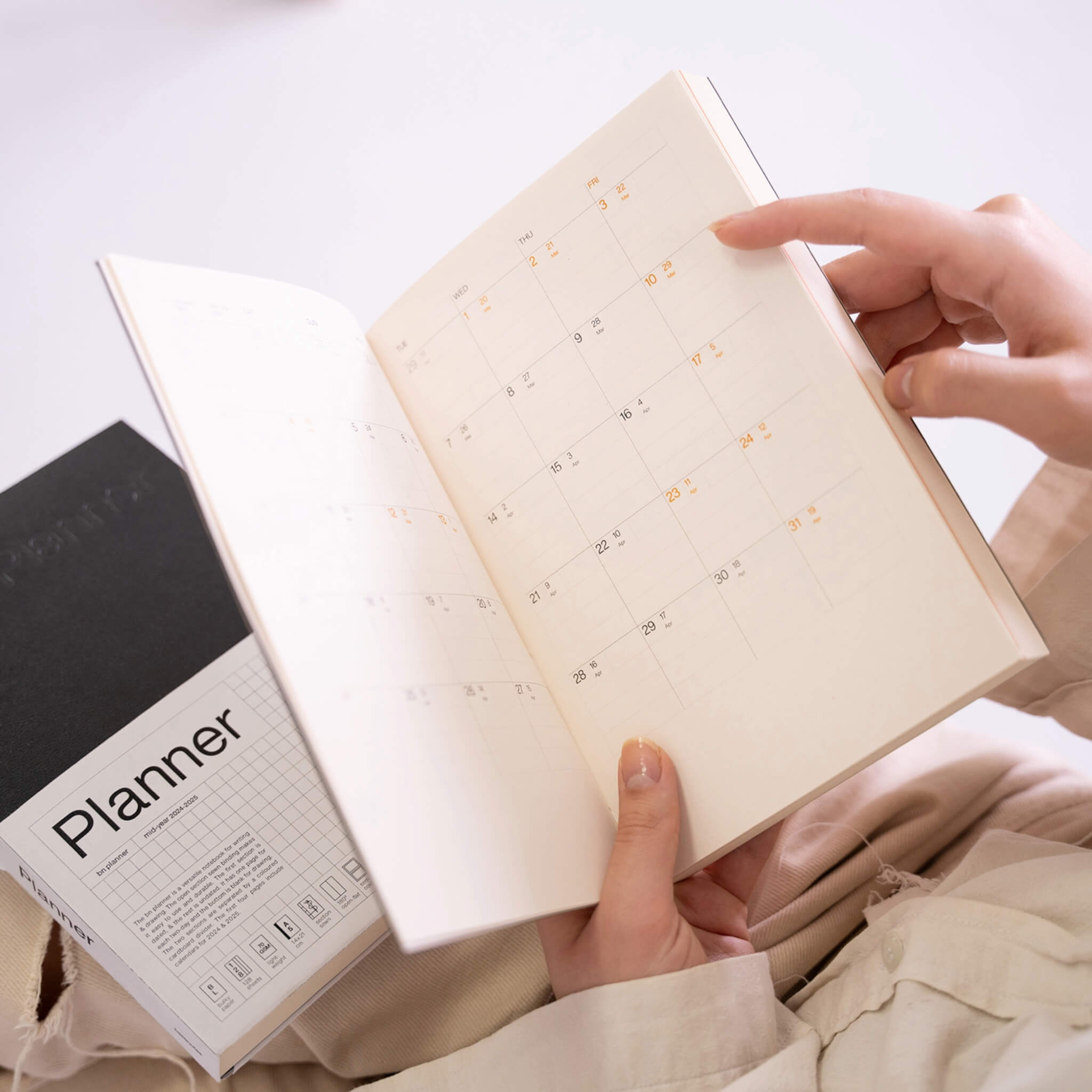 Person browsing the basenotes Planner, open on a monthly calendar page printed on softly textured FSC-certified paper for clear, minimal planning.