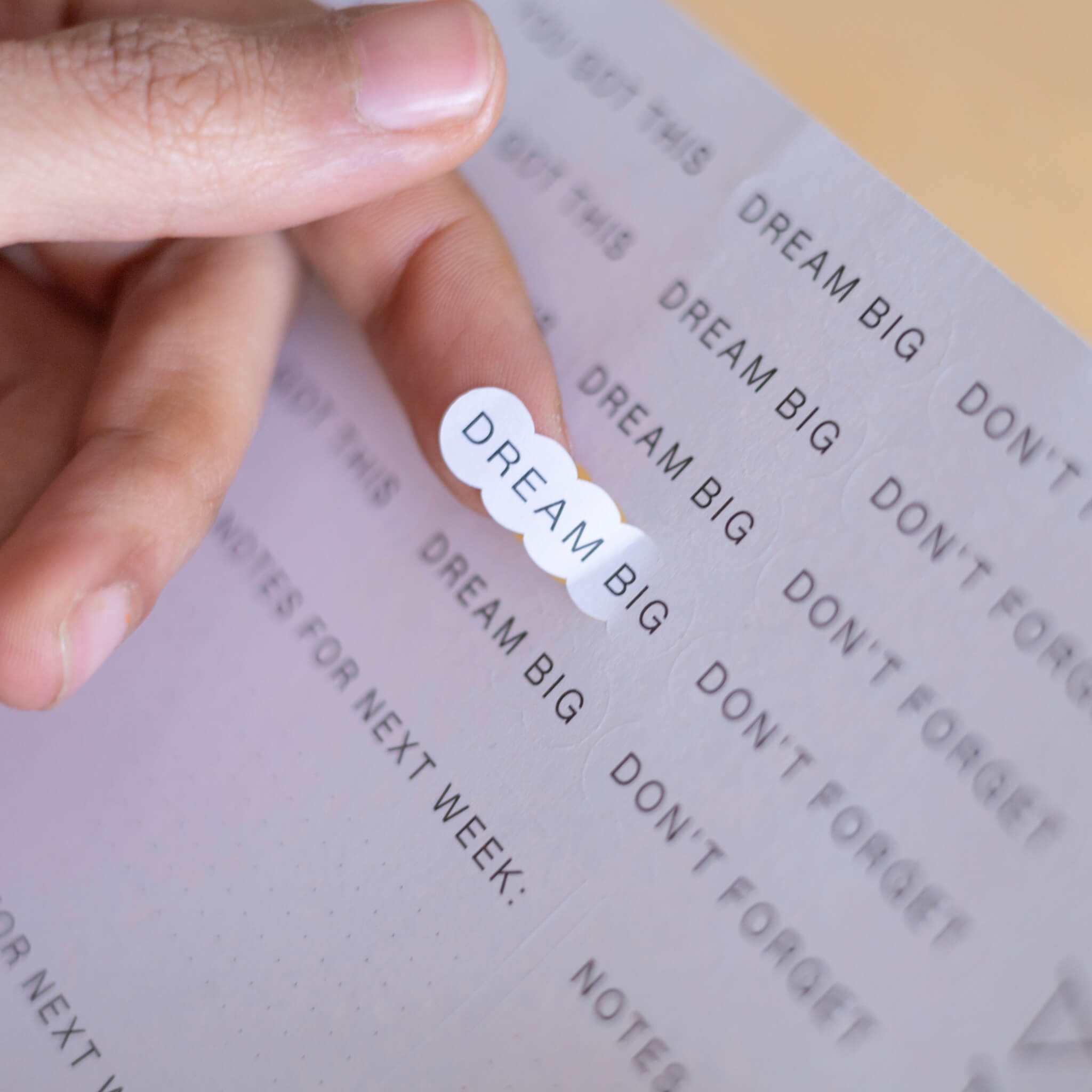 Hand peeling a “Dream Big” text sticker from a basenotes sticker sheet