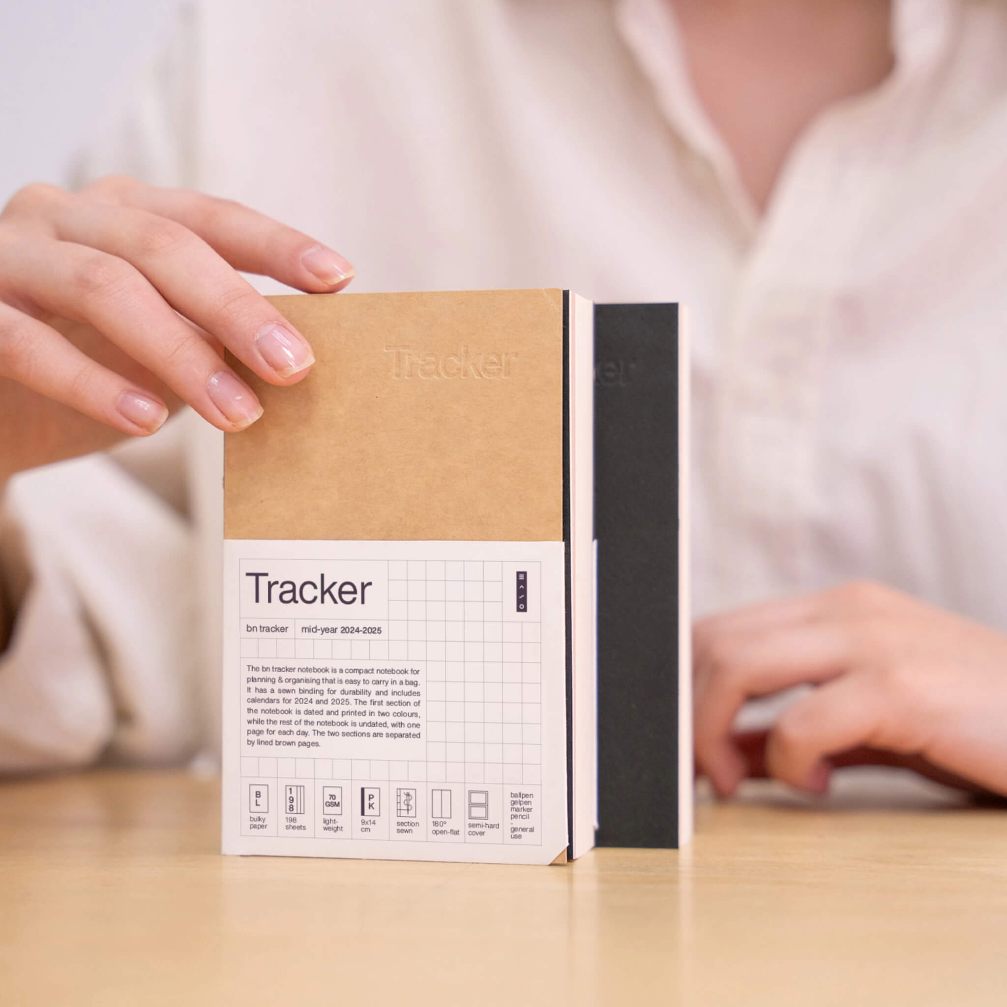 Kraft and black basenotes Tracker Notebooks displayed upright on a desk, featuring clean minimal packaging.